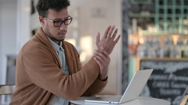 Kafede dizüstü bilgisayar kullanırken bileği ağrıyan Afrikalı bir adam 