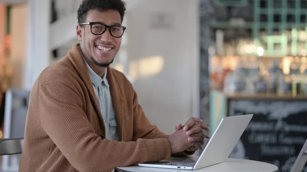 Αφρικανός με φορητό υπολογιστή χαμογελώντας στην κάμερα στο καφέ — Φωτογραφία Αρχείου