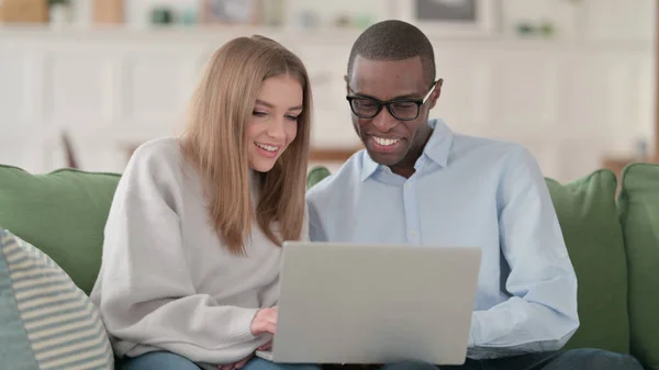 Casal Interracial animado enquanto trabalhava no laptop, casa — Fotografia de Stock