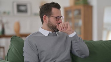 Orta yaşlı adam koltukta otururken öksürüyor.