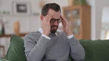 Orta yaşlı adamın koltukta otururken başı ağrıyor.