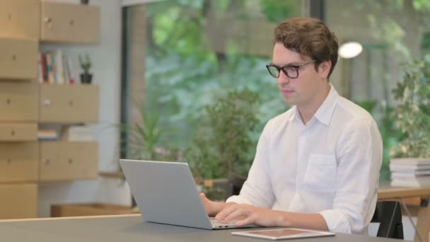 Giovane uomo che punta alla fotocamera durante l'utilizzo del computer portatile in ufficio moderno — Video Stock