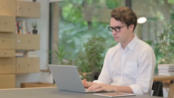 Hombre joven celebrando el éxito mientras usa el ordenador portátil en la oficina moderna — Vídeo de stock