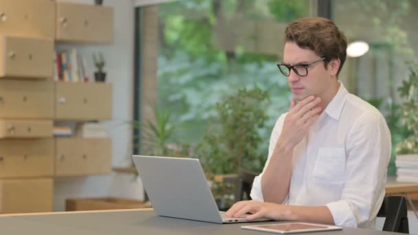 Jongeman denken tijdens het werken op Laptop in Modern Office — Stockvideo