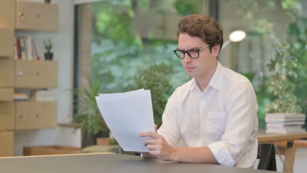 Jonge man die documenten leest terwijl hij in het moderne kantoor zit — Stockvideo