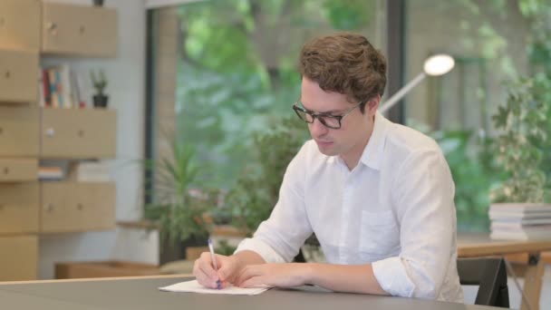 Jongeman schrijft op papier in het moderne kantoor — Stockvideo