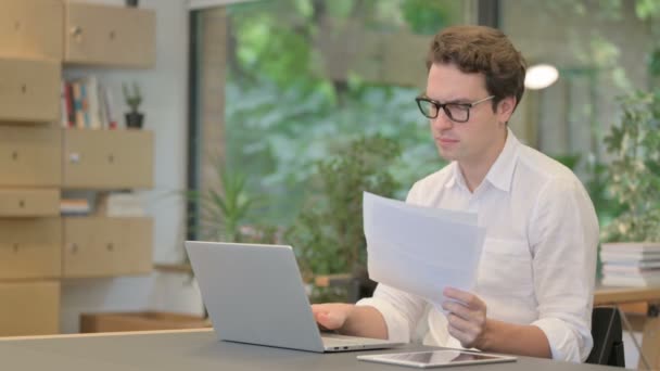 Mann mit Laptop liest Dokumente in modernem Büro — Stockvideo