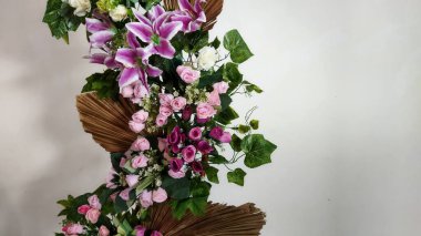 Pembe güller, beyaz zambaklar ve dekoratif kahverengi kağıtlarla süslenmiş yemyeşil yapraklardan oluşan canlı bir çiçek aranjmanı etkinliklere ve ev dekorasyonuna uygun yeni, zarif bir görünüm..