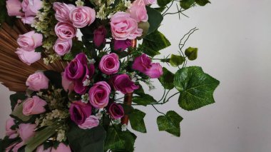 Canlı pembe ve mor gül buketi, yemyeşil yapraklarla bembeyaz arka planda düzenlenmiş çiçek ve hediye pazarlama için ideal taze ve neşeli bir atmosfer yaratıyor..