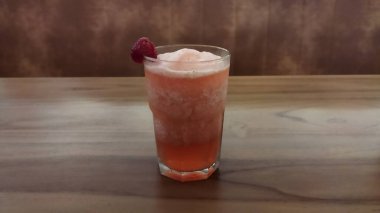 Tazeleyici pembe meyveli kokteyl ahududu garnitürle ahşap bir masada oturur ve canlı ve davetkar bir atmosfer yaratır. Bar veya parti pazarlaması için mükemmel..