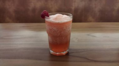 Soğuk, pembe bir meyve kokteyli ve ahududu süslemesi ahşap bir masada berrak bir bardakta yenilenmiş ve canlı bir atmosfer yaratır. Günlük yemek ve içecek pazarlaması için ideal..