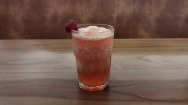 Soğuk ahududu kokteyli, köpüklü üst ve ahududu garnitürlü ahşap masa, içecek ve konukseverlik pazarlaması için ideal, ferahlatıcı ve davetkar bir atmosfer yaratır..