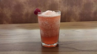 Buzlu buzlu soğuk pembe meyve kokteyli ve ahşap bir masada berrak bir bardakta meyveli garnitür gündelik yemek ve yaz ferahlığı için mükemmel ferahlatıcı ve canlı bir atmosfer yaratır..