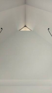 Çağdaş iç tasarım için uygun modern ve sakin bir atmosfer yaratarak doğal ışığın mekanı aydınlatmasına olanak sağlayan üçgen bir çatı penceresi olan temiz beyaz bir tavan..