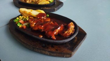 Mangal sosuyla kaplanmış lezzetli bir tavuk budu arka planda karışık sebzelerle birlikte siyah taştan bir tabakta servis edilir. Yemek menüleri ve mutfak pazarlama için mükemmel ve cazip bir sunum yaratır..