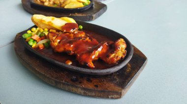 Izgara tavuk ve parlak barbekü sosu arka planda karışık sebzelerle birlikte koyu taş tabakta servis edilir. Yemek ve yemek pazarlama için mükemmel, davetkar bir ortam yaratır..