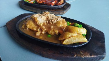 Sos soslu sıcak tavuklu turta, çıtır patates dilimleri ve iştah açıcı sunum için koyu ahşap bir tabakta servis edilen yeşil bezelye..