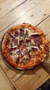 Eritilmiş peynirli ve çıtır çıtır bir pizzayla ahşap bir masada dinlenen sıcak, taze, fırınlanmış bir pepperoni peyniri yemek pazarlama için mükemmel bir yemek atmosferi yaratır..