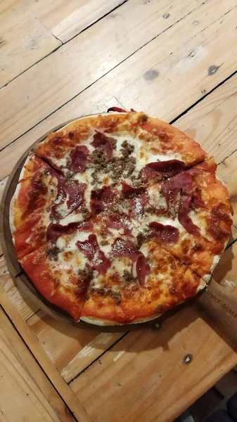 Eritilmiş peynirli ve çıtır çıtır bir pizzayla ahşap bir masada dinlenen sıcak, taze, fırınlanmış bir pepperoni peyniri yemek pazarlama için mükemmel bir yemek atmosferi yaratır..