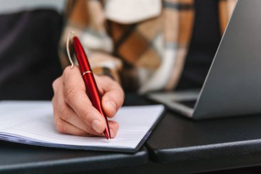 Bir kadın kırmızı tükenmez kalemle deftere bir not yazıyor. Yakın plan fotoğraf.