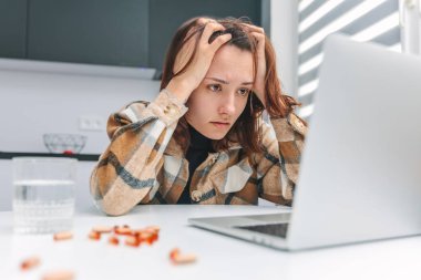 Evde dizüstü bilgisayar kullanarak çalışan yorgun bir kadının portresi. Kız stres yüzünden başını tutuyor.
