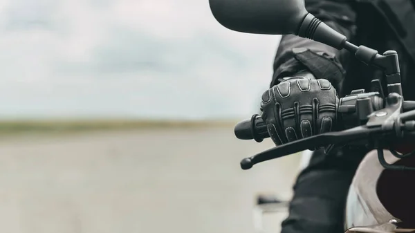 Hand of a man in protective motorcycle gloves holds a black motorcycle, close up