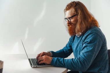 Masada dizüstü bilgisayarda çalışan kızıl saçlı adam.