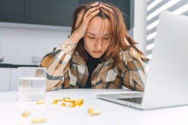 Depresyondaki kadın evde dizüstü bilgisayarda çalışıyor ve haplar masada yatıyor.