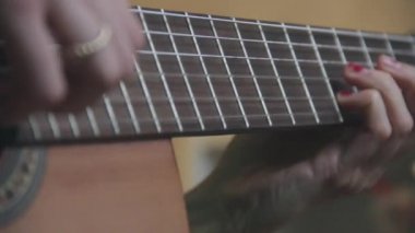 Kadın elleri akustik gitar çalıyor, yakın çekim.