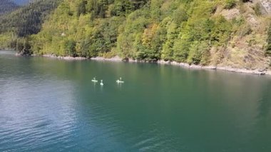 Dağ Gölü 'nün hava aracı görüntüsü ve insanlar gün batımında sörf tahtasında kürek çekiyorlar. Su sporu yapan üç arkadaş yaz tatillerini birlikte geçiriyorlar. Aktif turizm ve seyahat kavramı.