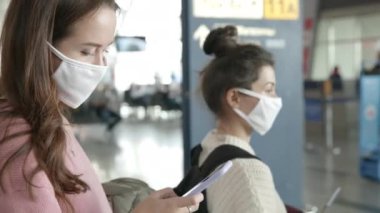 Koruyucu maskeli insanlar uçağa binmek için sırada bekliyorlar. Havaalanı terminalinde bekleyen iki kadın kendilerini koronavirüsten koruyor. Salgın covid-19 kavramı.