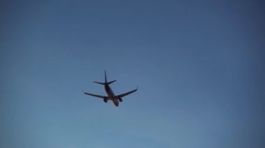 Akşam gökyüzünde uçan uçağın silueti. Gün batımında gideceği yere giden hızlı bir uçak. Turizm, ulaşım, tatil kavramı.