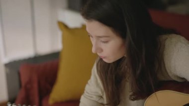 Genç Asyalı kadın evde gitar çalıyor. Müzisyen olmak isteyen biri dizüstü bilgisayarla müzik aleti çalmayı öğreniyor. Evde tek başına takıl. Güzel kız online ders izliyor ve müzik çalışıyor.