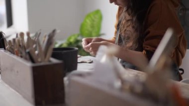 Profesyonel çömlekçi kadın bir kil el sanatının ayrıntıları üzerinde çalışıyor. Farklı çömlek aletleriyle çalış. Yaratıcı eğlence zamanı ve seramik kavramı. Küçük bir iş, sanat eseri ve iç mekan kuracağız.