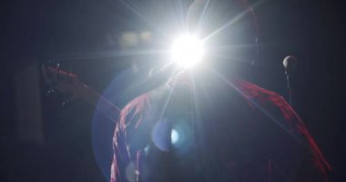 Karanlık konser salonunda gitar çalan erkek silueti. Siyahi müzisyen arkada durup performans sergiliyor. Kayıt stüdyosundaki adamın izole edilmiş arka görüntüsü. Rock grubu konsepti