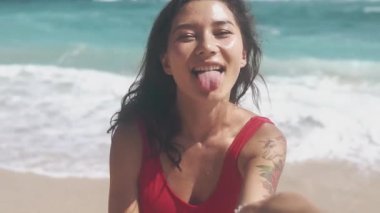 Sahilde güzel bir kadının portresi beni takip et. Okyanusta kırmızı mayosuyla poz veren seksi kadın. Çekici esmer kadın kameraya gülümsüyor dalgaların ve kumların arkasında..