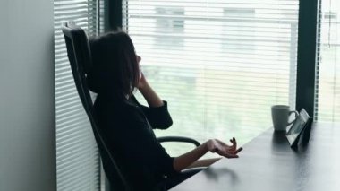 Ofiste çalışan ve telefonda konuşan genç iş kadınının portresi. Kadın girişimci ciddi bir konuşma yapıyor, durumu çözmeye ve çözüm bulmaya çalışıyor. Bağımsızlık kavramı, teknoloji,