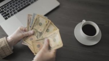 Ödeme, finans konsepti. Dolar banknotları olan kadın elleri. Koruyucu eldivenli bir kadın, kafedeki masada para sayıyor ve çalışıyor. Para ve kazançlar