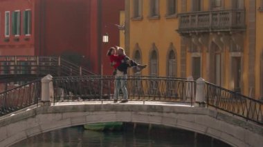 Yakışıklı bir adam, balayı sırasında Venedik köprüsünde duran Asyalı sevgilisini öpüyor ve sarılıyor. Tatili geçirmenin en iyi yolu Avrupa 'ya seyahat etmek..