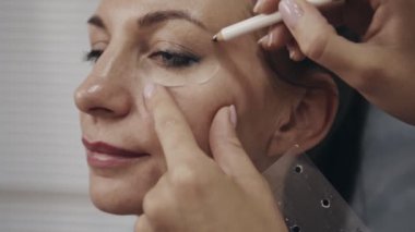Kadın yüzünün kozmetologla yakın plan portresi güzellik prosedürüne hazırlanmak için düzeltme çizgileri çiziyor. İşlemden önce uzman işaretleme noktaları.