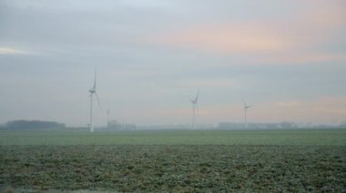 Sisli bir günde yeşil çayır ve yel değirmenlerinin havadan panoramik manzarası. Rüzgar türbinlerinin muhteşem manzarası güzel ovalarda enerji üretiyor..