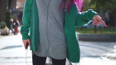 Renkli saçlı çekici bir genç kadın kulaklıkla müzik dinliyor, dans ediyor, akıllı telefon kullanıyor ve şehir müziğinde yürüyor. Parlak görünüşlü gülümseyen kız aletler kullanıyor..