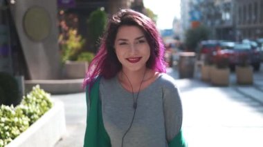 Parlak görünüşlü gülümseyen kız aletler kullanıyor. Renkli saçlı çekici genç bir kadın kulaklıkla müzik dinliyor, akıllı telefon kullanıyor ve şehir içinde yürüyor..
