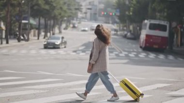 Kırmızı ışıktan hemen önce bir kız zıplıyor, karşıya geçiyor. Elinde bavulla yaya geçidinde koşan genç bir kadın. Güneşli bir günde etrafa bakıp gülümseyen bir kadın. Yaşam tarzı kavramı, seyahat.