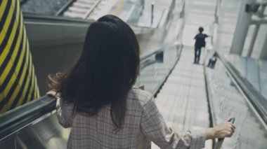 Havaalanında yürüyen merdivenden inen genç bir iş kadını. Güzel bir kadın bagajıyla hareket ediyor, terminale bakıyor. İş gezisi için uçağa binen bir kız. Seyahat ve iş kavramı.
