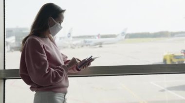 Havaalanı terminalinde maskeli yalnız bir kız silueti uçuş öncesi uçak biletiyle birlikte. Coronavirus önleme konsepti. Pandemik zamanda yolculuk.