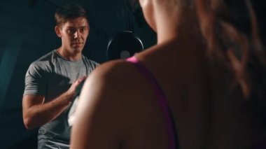 Genç esmer boksör ve antrenör. Atletik kız antrenörle tek başına çalışıyor. Erkek ve kadın kardiyo çalışması yapıyor. Adam kıza antrenman için yardım ediyor. Antrenman, güç, spor salonu kavramı.