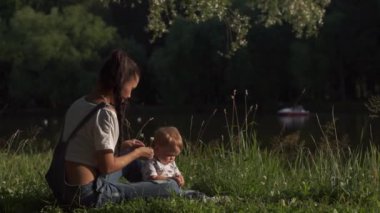 Doğanın güzelliğini yaşayan çocuk: yeşil ağaçlar, kuşlar ve su. Anne ve oğlu parkta göletin kenarında oturuyorlar. Toddler annenle el çırpmaya çalışıyor, etrafa bakıyor. Annelik kavramı
