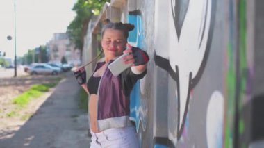 Yaratıcı kız sanatçı. Kültür özgürlüğü, tatil, yaşam tarzı konsepti. Genç ve güzel hippi kız sıcak yaz gününde şehrin banliyösünde grafiti duvarının önünde cep telefonuyla selfie çekiyor.