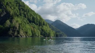 Gün batımında dağ eteğinde yemek güvertesinde sörf yapan iki kadın. Yaz tatili boyunca bayan arkadaşlar. Resimli bir manzara. Spor ve turizm konsepti.